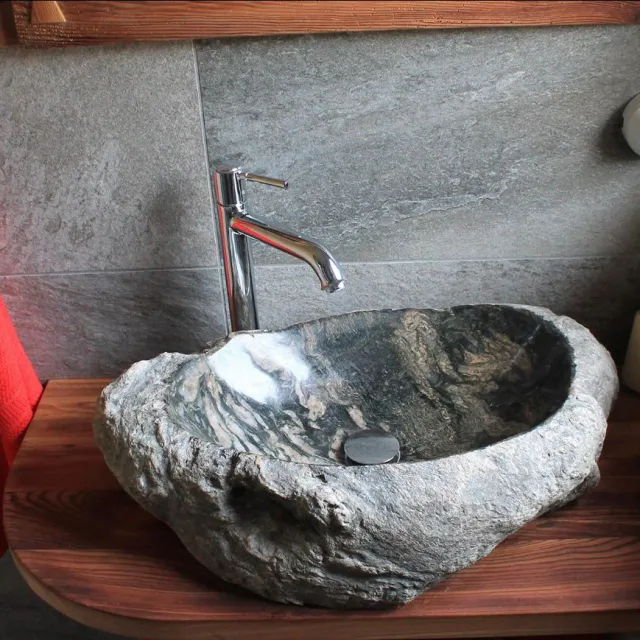 Lavabo in pietra naturale con rubinetteria cromata davanti a piastrelle in pietra